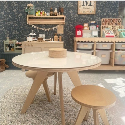 Mesa redonda branca com pés de madeira clara e banco redondo no quarto infantil com móveis em madeira e objetos coloridos