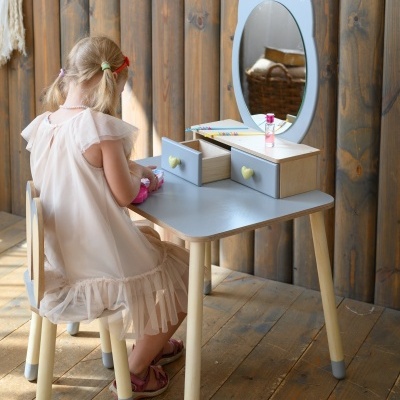 Mesa infantil cinzenta com espelho decorado e criança sentada de costas