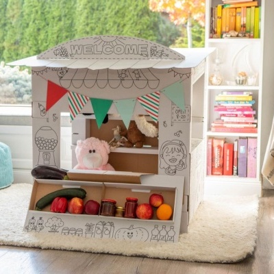 Casinha de brincar de cartão com decoração e frutas falsas num quarto acolhedor.