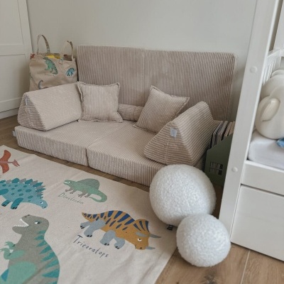 Sofá infantil bege em tecido veludo cotelê com almofadas e tapete de dinossauros no chão