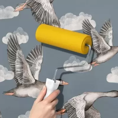 Rolo de pintura amarelo a pintar papel de parede com padrão de gansos voadores e nuvens