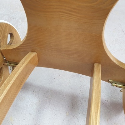 Vista inferior de mesa pequena de madeira clara com pernas curvas e rodas com recortes