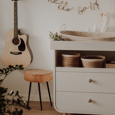 Quarto com guitarra acústica, banco de madeira, cómoda branca com cestos, berço de vime e móbile HELLO BABY