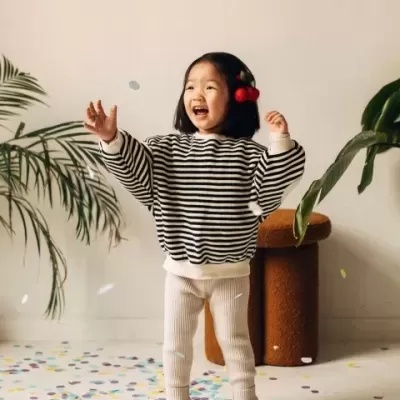 Criança sorridente com roupa listrada e calças bege rodeada por confetes e plantas