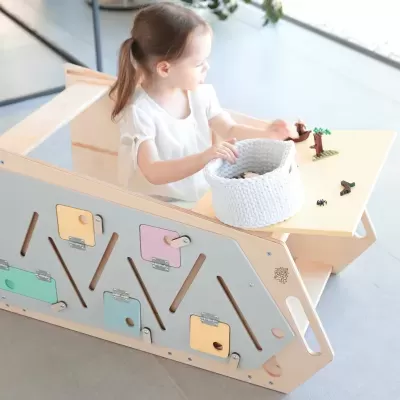 Mesa e banco de madeira clara com painel multi-atividades e cesto branco, com criança a brincar.