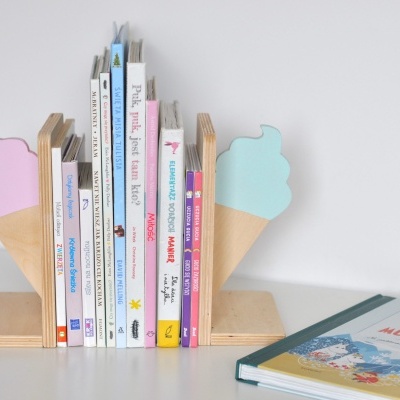 Suporte de livros em madeira decorado com gelados e livros infantis variados numa mesa branca.