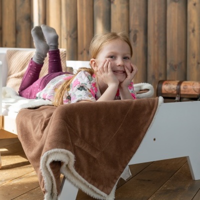 Cama infantil branca com criança deitada e manta castanha