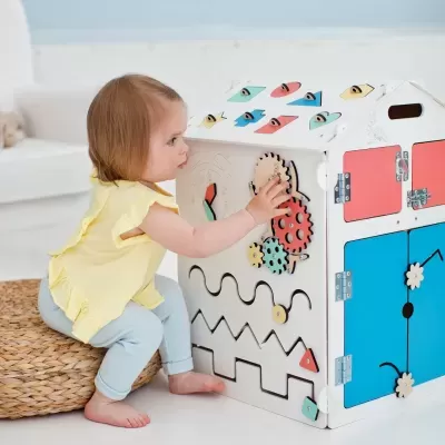 Criança a brincar com brinquedo educativo de madeira em forma de casa com várias atividades