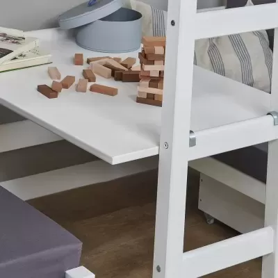 Mesa branca com brinquedo de peças de madeira empilhadas e livros sobre mesa com cadeiras brancas e almofadas cinzentas