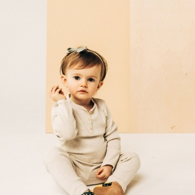 Bebé sentado com macacão bege e sapatos marrons e azuis com flores.