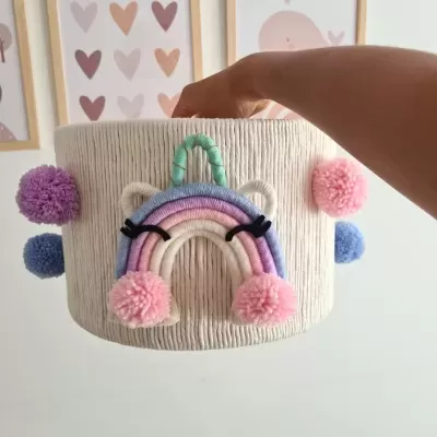 Cesta de tecido creme com decoração de arco-íris e pompons coloridos