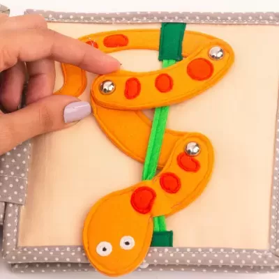 Livro de tecido com figura de cobra em feltro laranja e verde com fecho metálico.