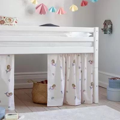Cama infantil branca com cortinas decorativas de sereias e ambiente com decoração colorida