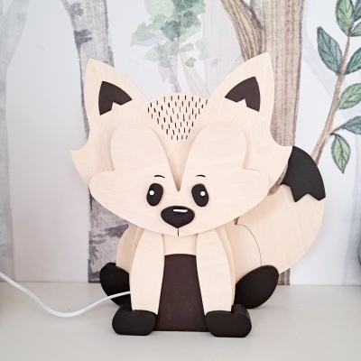Luminária infantil de madeira em forma de raposa, bege e preta, em cima de mesa com parede desenhada ao fundo
