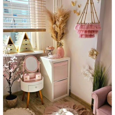 Canto decorativo com móveis brancos e rosa, tapetes, flores e luminária pendente rosa com franjas.