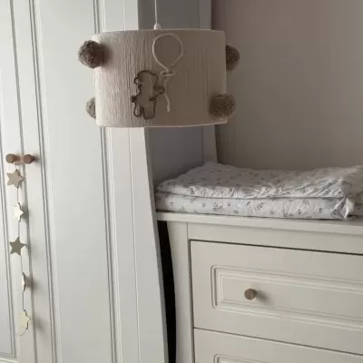 Candeeiro de teto infantil decorado com ursinho e pompons, junto a móveis brancos