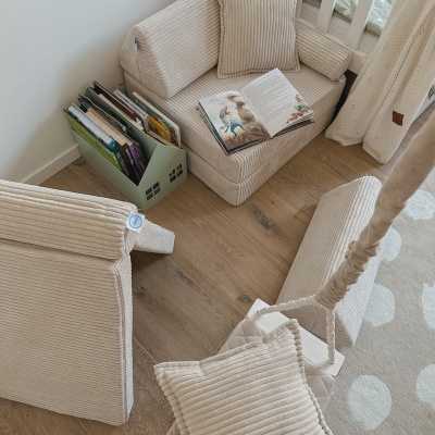 Espaço infantil com cadeirão e sofá em tecido canelado bege, almofadas e estante de livros em forma de casa