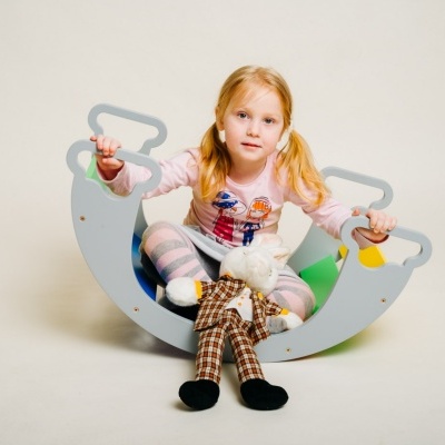 Menina loira sentada num baloiço colorido com pijama e boneco de peluche