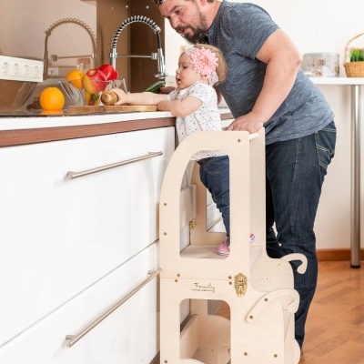 Torre de aprendizagem infantil de madeira clara em cozinha moderna com bancada branca e frutas