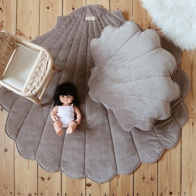 Tapete cinzento em formato de folha com almofada, cadeira de vime e boneca sobre piso de madeira