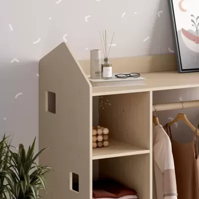 Móvel de madeira clara com estantes e barra para pendurar roupa, acessórios em cima, parede bege com padrão branco.