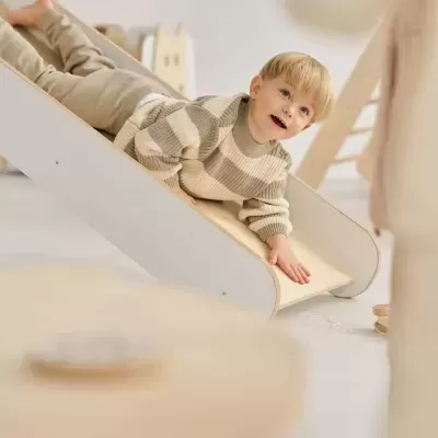 Criança a deslizar num escorrega de madeira clara e branco