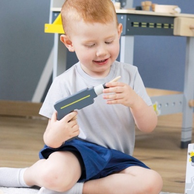 Criança sentada no chão a brincar com ferramenta de brinquedo cinzenta e amarela