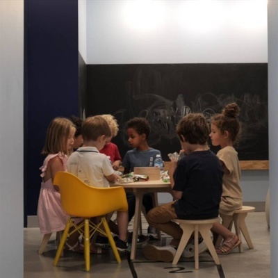 Crianças sentadas à mesa num ambiente interior com parede de ardósia preta