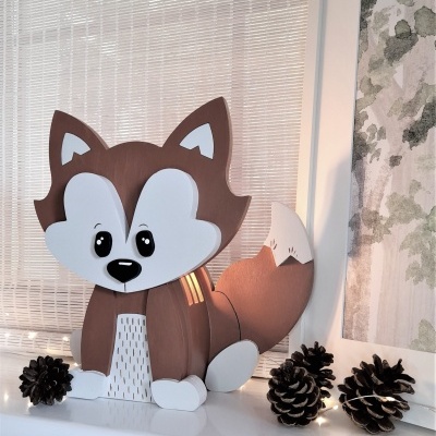 Figura decorativa de raposa em madeira ao lado de pinhas e luzes