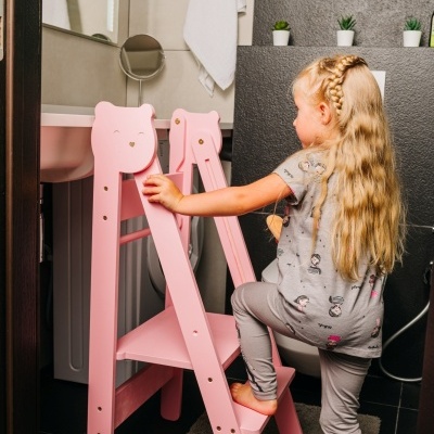 Criança a subir escada de aprendizagem rosa em banheiro com paredes cinzentas