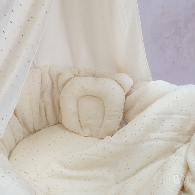 Berço branco acolchoado com pequenos pontos dourados e almofada de urso