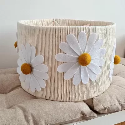 Cesto tecido creme com flores brancas e centro amarelo sobre almofada bege