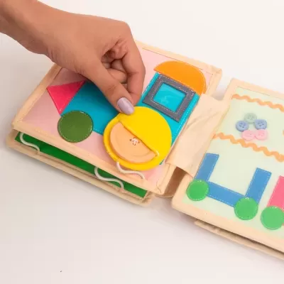 Livro infantil de tecido colorido com formas geométricas e botões num fundo branco