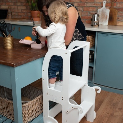 Criança em escada de madeira branca junto a mesa de cozinha com mulher
