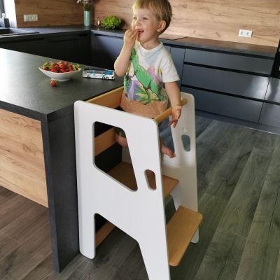 Torre de aprendizagem branca e madeira numa cozinha moderna com criança sentada