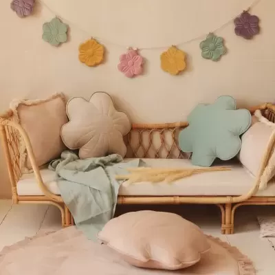 Sofá de vime com almofadas florais e lisas em tons pastel e guirlanda de flores coloridas na parede