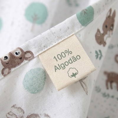 Etiqueta de tecido com texto 100% Algodão em tecido branco com desenhos de animais e árvores.