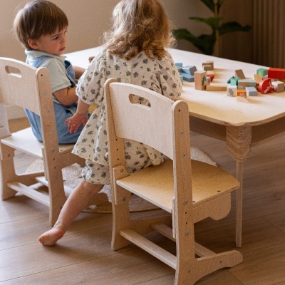 Crianças sentadas em cadeiras de madeira clara diante de mesa baixa com blocos de madeira coloridos