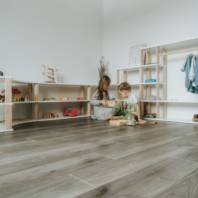 duas crianças brincam no chão junto a estantes de madeira com brinquedos e roupas