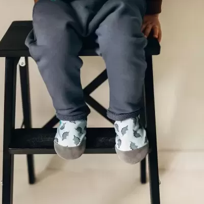 Calçado infantil com padrão de dinossauros cinzentos e fundo azul claro usado por criança sentada