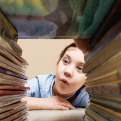 Criança olhando entre pilhas de livros amarelados em ambiente interno