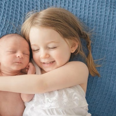 Criança abraçando recém-nascido deitado sobre manta azul
