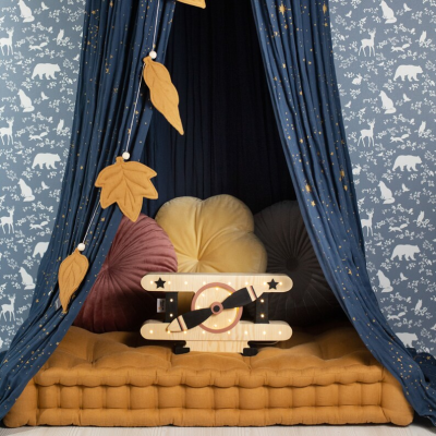 Espaço infantil com colchão amarelo, cortina azul estrelada, almofadas coloridas e avião de madeira