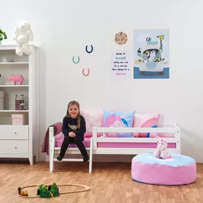 Quarto infantil com cama branca, almofadas coloridas, pufe e peluche, brinquedo de madeira e decoração na parede