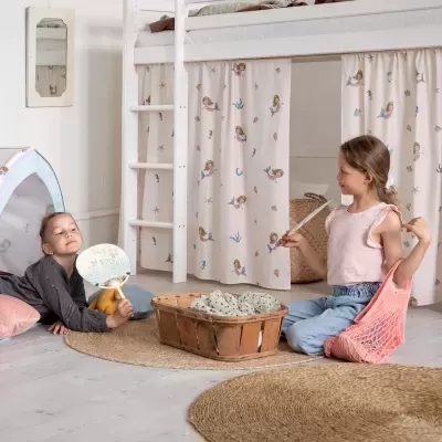 Quarto infantil com cama alta, cortinas de sereia, tapete redondo, cesta de madeira e duas crianças a brincar