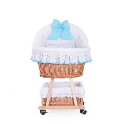 Berço de bebé em vime decorado com tecido branco e azul, com estrutura em madeira clara e rodas.