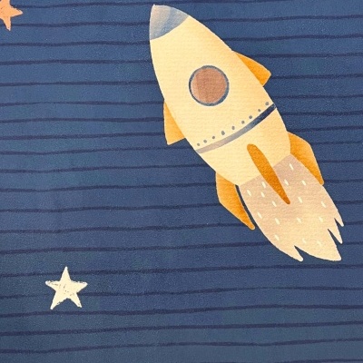 Pano azul com desenho de foguetão amarelo-alaranjado e estrelas