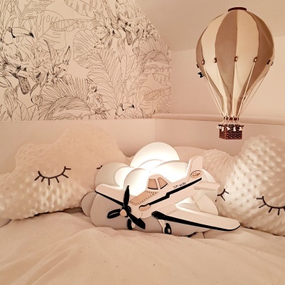Almofadas nuvem e rosto com olhos fechados, lâmpada avião e balão ar quente em quarto infantil