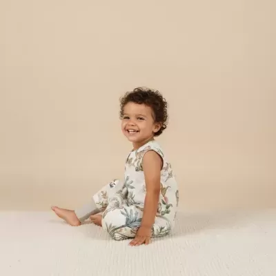 Criança sentada a sorrir com fato estampado de plantas e animais em fundo bege