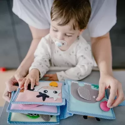 Livro de pano colorido para bebé com imagens de animais e texturas interativas.